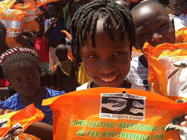 Children smiling and holding up mosquito nets