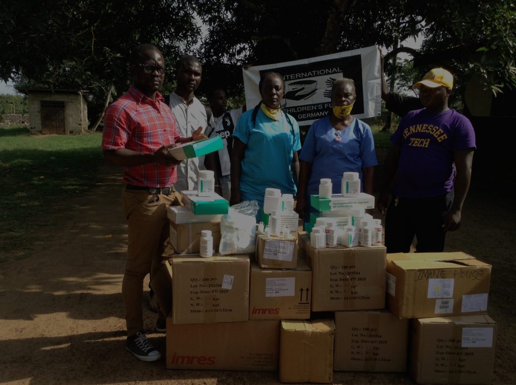 Group of healthcare workers standing beside boxes of medical supplies, including medications and equipment, in a community setting. The background features a banner for the International Children's Fund, highlighting the provision of essential healthcare resources.