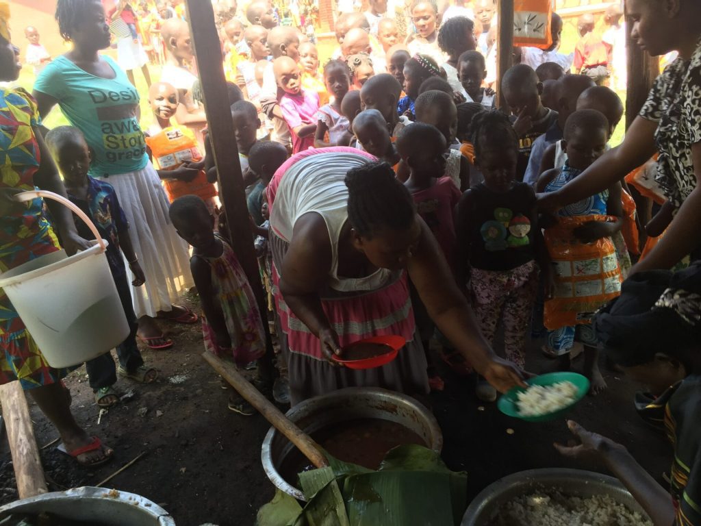A community gathering where volunteers serve food to a group of children, showcasing a charitable event focused on providing meals. The scene captures adults distributing rice and stew while children eagerly wait in line, highlighting community support and engagement.