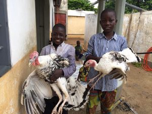 Two boys smiling while holding turkeys in a rural setting, showcasing local farming practices and community life.