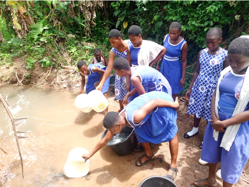Group of schoolgirls in blue uniforms collecting water from a stream, highlighting the importance of water access and community engagement in rural areas.