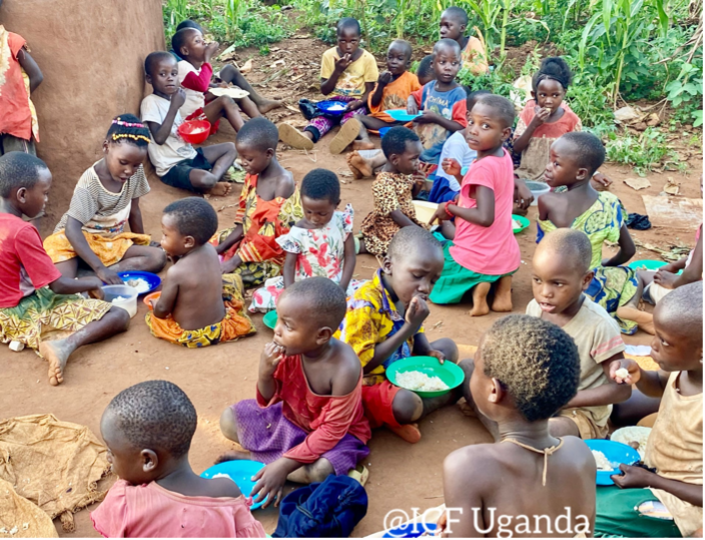 Children in Uganda enjoying a communal meal outdoors, sitting on the ground with colorful bowls of food, surrounded by greenery.