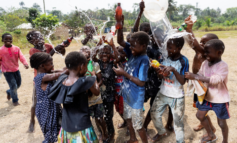 Children joyfully playing with water outdoors, celebrating and splashing water on each other in a natural setting, showcasing happiness and community spirit.