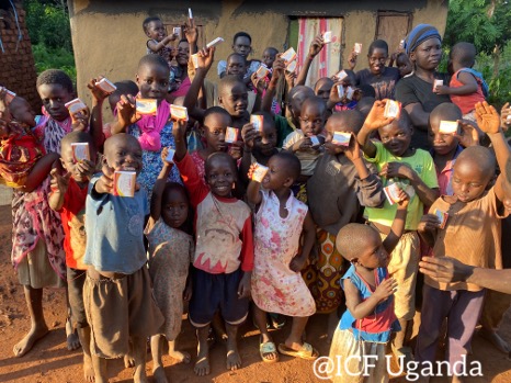 Group of children in Uganda joyfully holding up health supplements outside a rural home, showcasing community support and engagement in health initiatives.