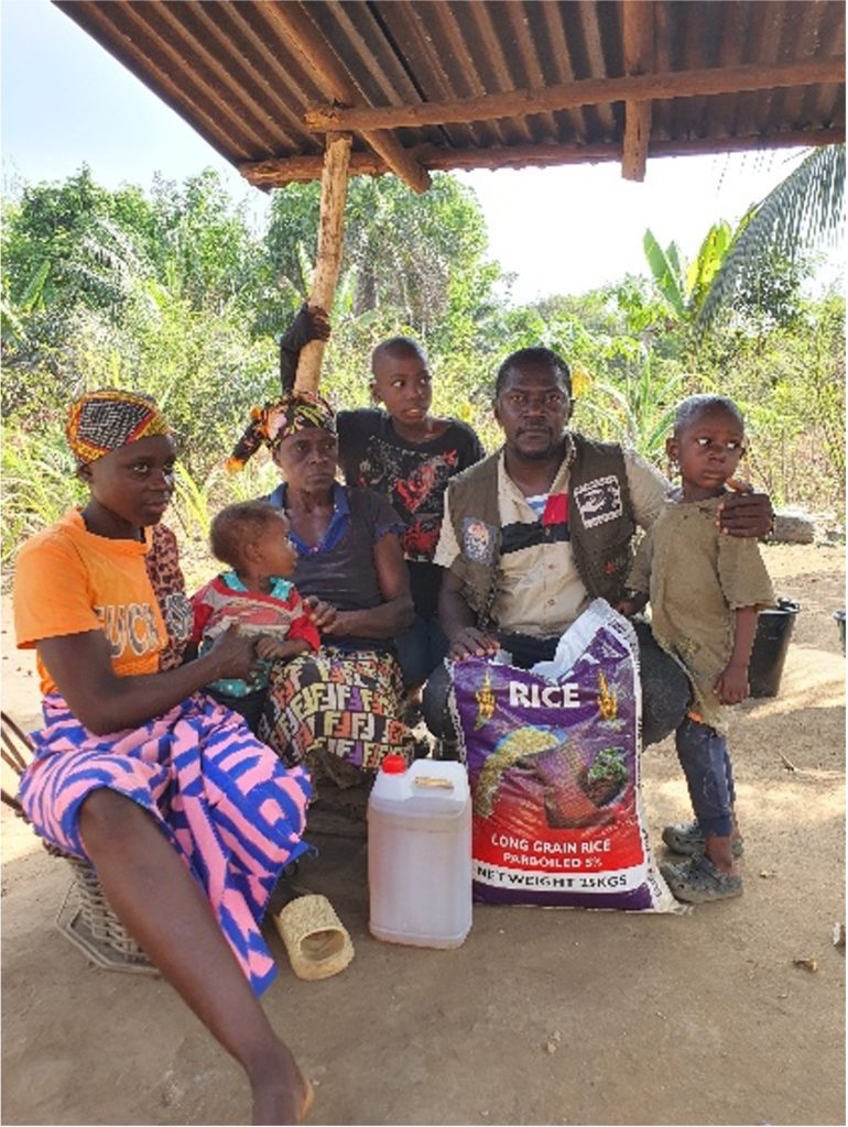 Family sitting with rice under a wooden shelter.